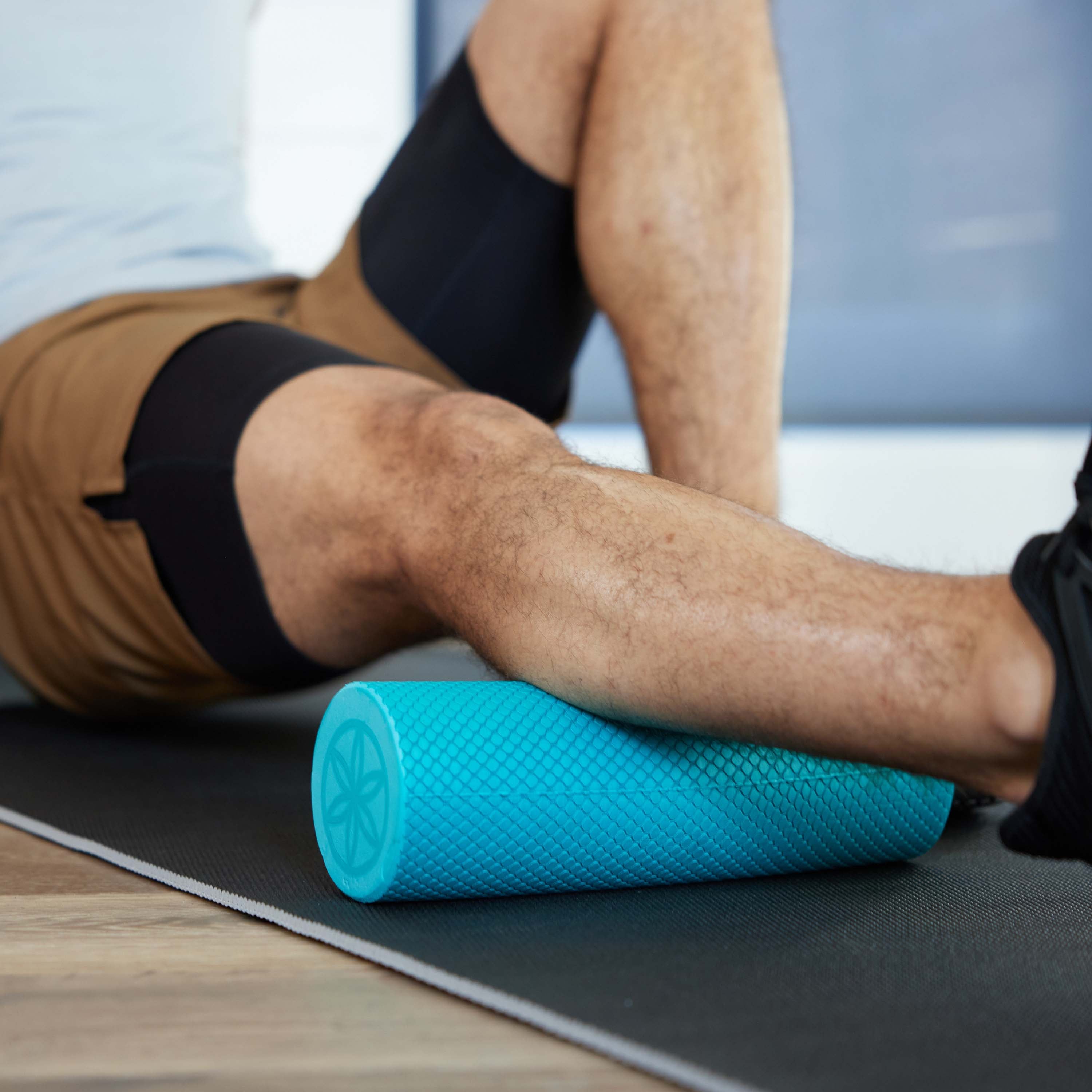 Up close of persons leg on yoga mat with the  Restore Compact Foam Roller under the calf